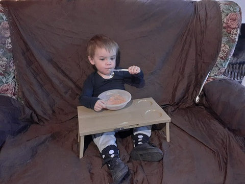 toddler boy sitting in front of the tv eating from the picnic tray