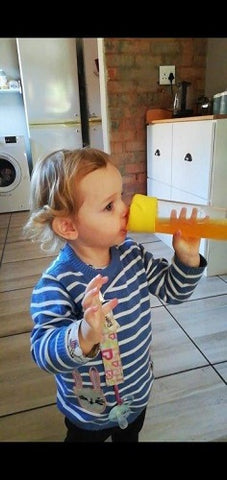 toddler sipping from a yellow portable juice blender in the kitchen