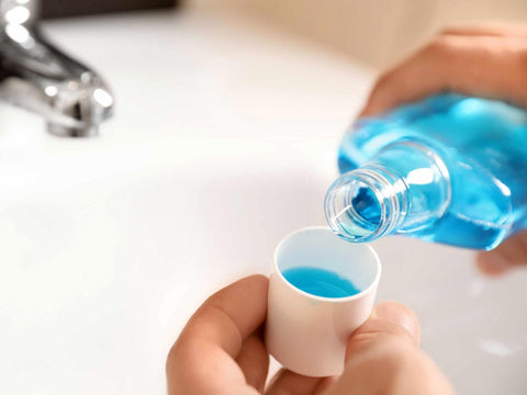 Blue mouthwash being poured from a bottle into a bottle cap