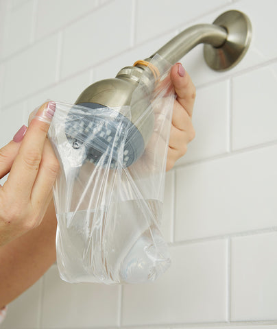 Plastic bag containing vinegar being tied around a shower head