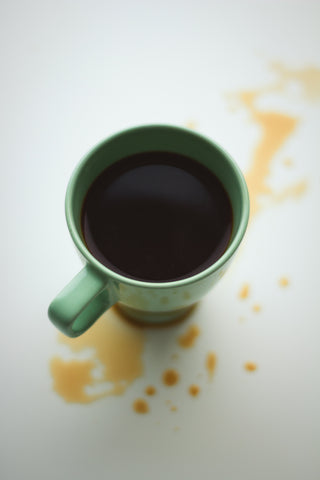 Spilled coffee around a green mug containing coffee