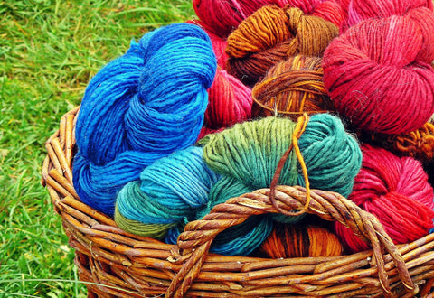 Colourful rolls of wool in a brown basket on the grass