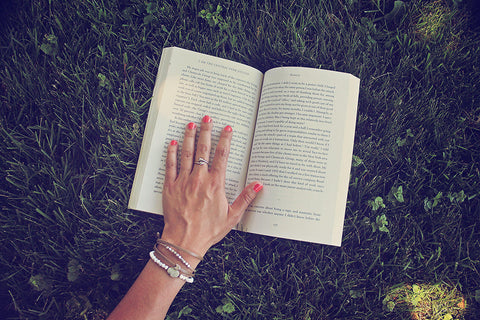2021 summer reading list - hand on book, wearing bracelets by Peacock and Lime