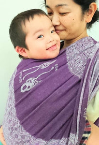 紫のベビーラップにママに密着してにこにこしているダウン症の赤ちゃん