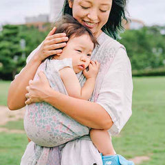 2歳ごろの子どもをパステル調のベビーラップで抱っこし、慰めているお母さん