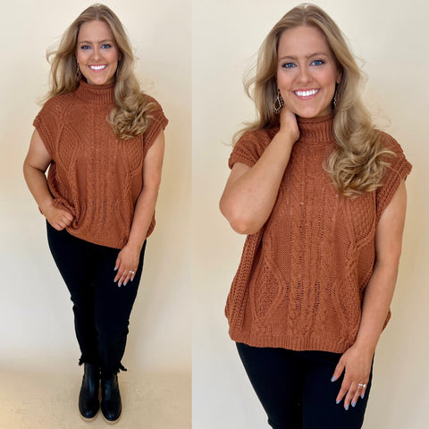 plus size camel colored high neck sweater vest. Sweater vest has a cable knit pattern on front. sweater is paired with black jeans and black boots