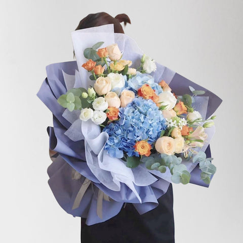 A bouquet of blue hydrangeas, orange roses and white roses