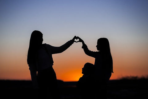 Silhouettes of two girls forming a heart and a girl sitting down