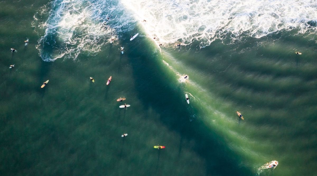 Drone photograph over a breaking wave with crowded surf lineup by photographerCate Brown