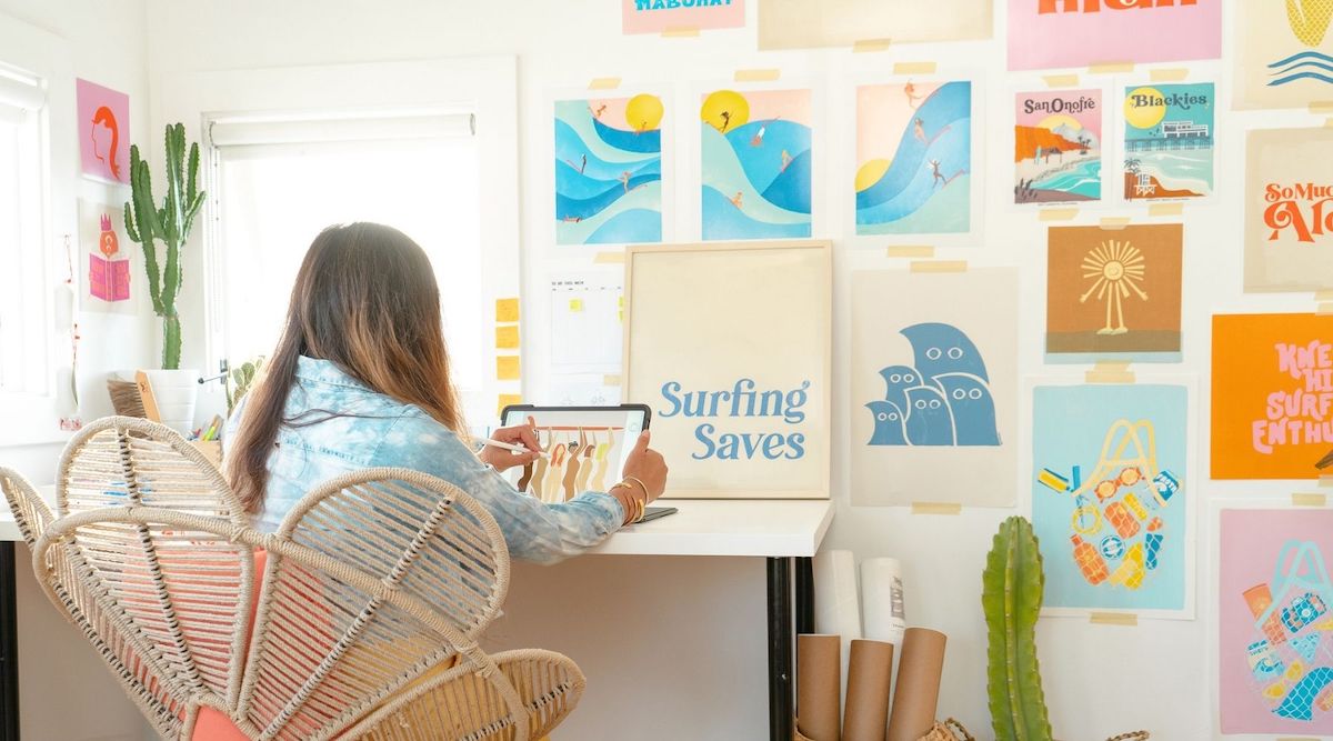 Janina Casanova female surf artist sketching at her desk in her creative studio with beautiful and bright surf art on the walls