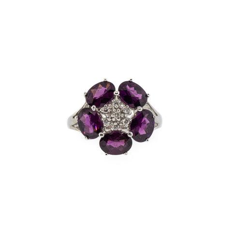 Deep purple oval rhodolite garnet petals surround a cluster of diamonds in a flower design. The ring is set in 14kwg