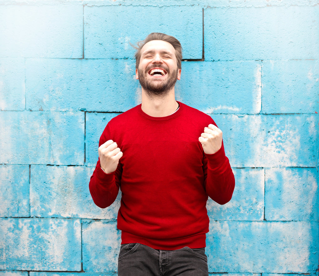 Adult man in red sweater smiling in front of a blue wall