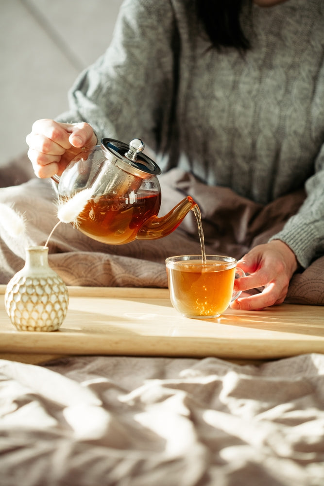 Woman pours tea into glass mug from teapot