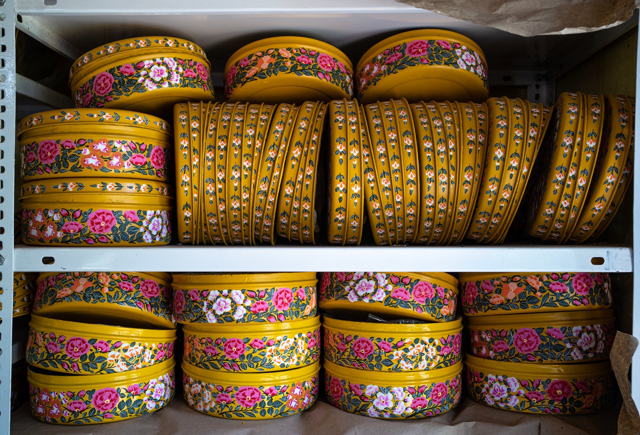 Rows of hand painted Cookie Tins stacked on 2 shelves 