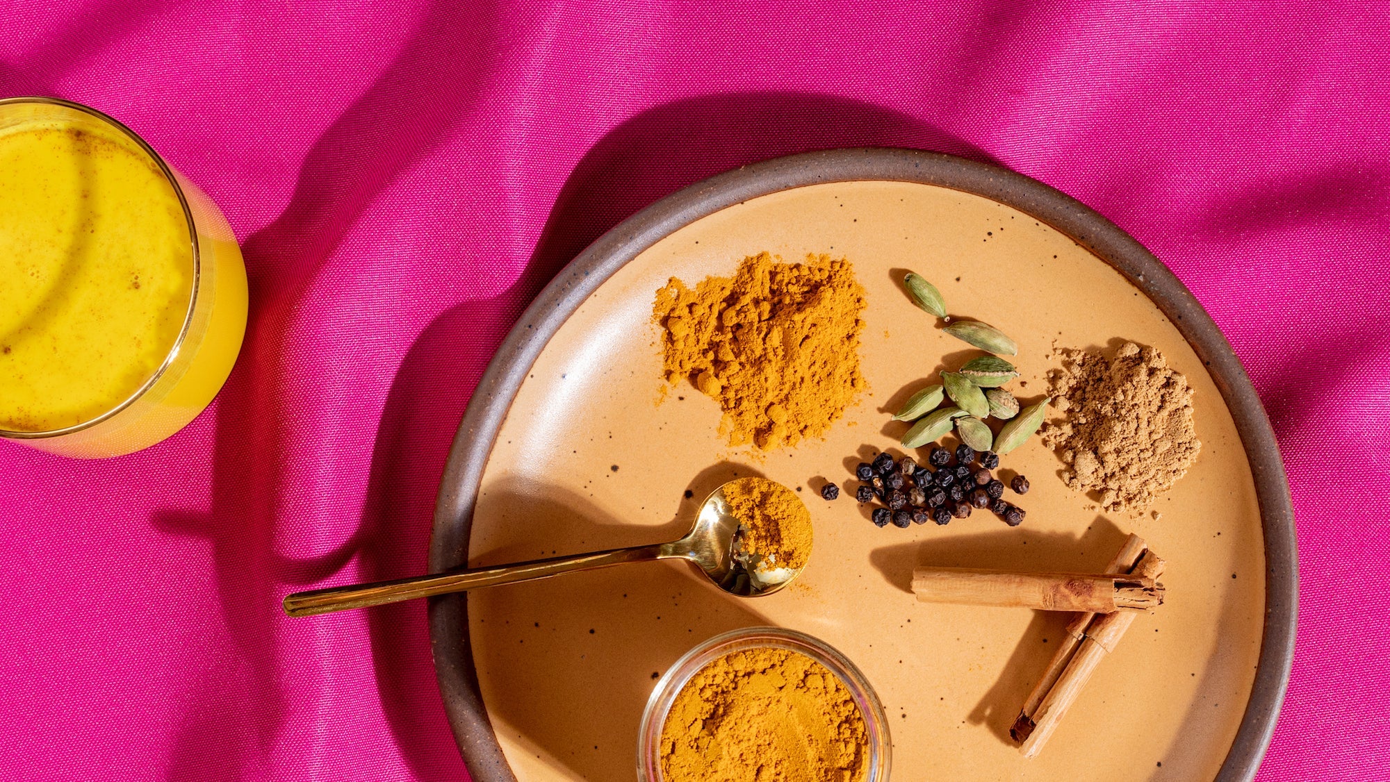 Cup of Haldi Doodh with a plate of the spices involved on a pink cloth background