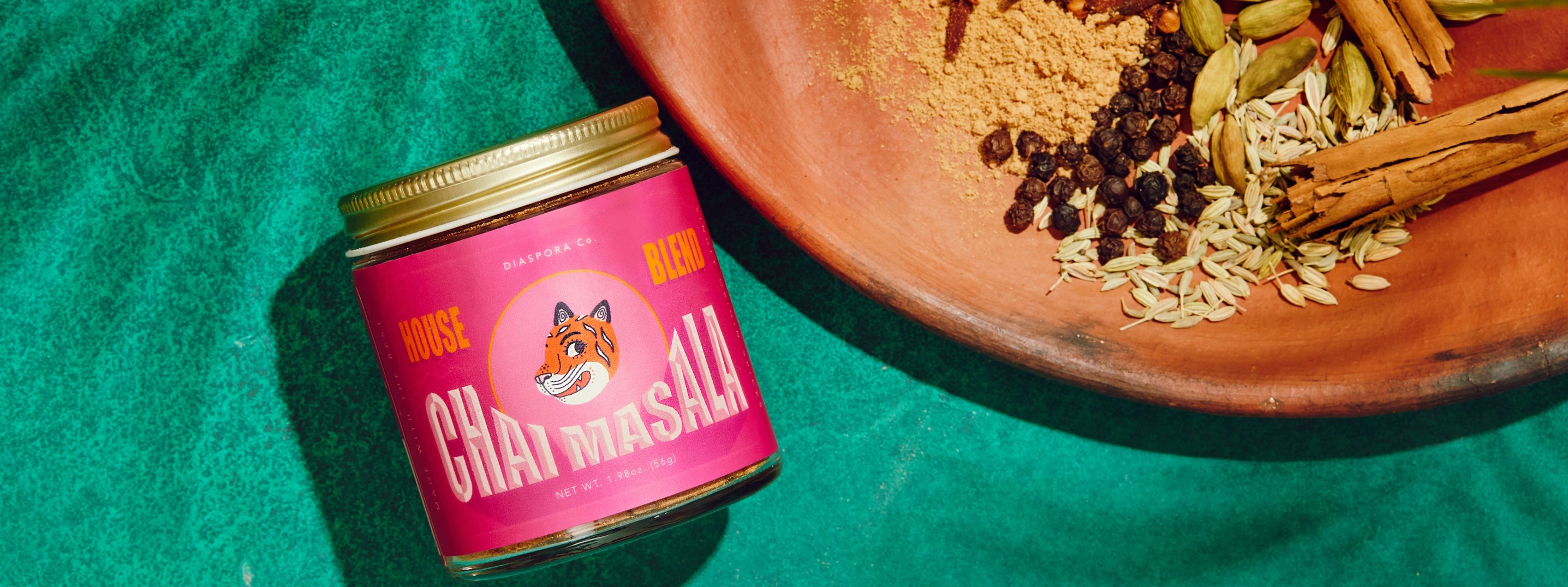 Photo of pink chai masala jar and chai spices on a clay plate, all on a teal background