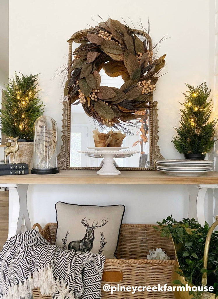 Two artificial cedar trees decorated on a shelf next to an artificial wreath