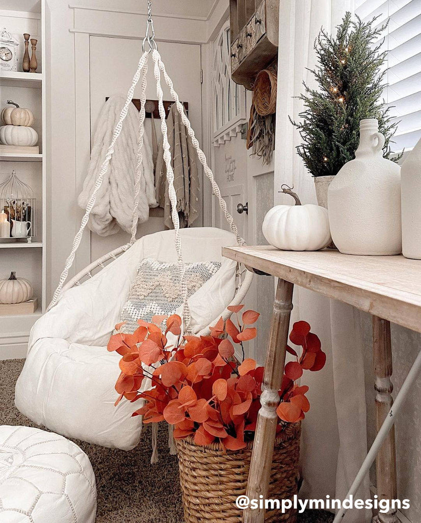 Artificial plant with orange leaves decorated inside a basket next to a hanging porch swing