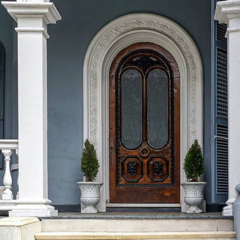 Two small artificial trees in a white urn decorated next to a large wooden front door