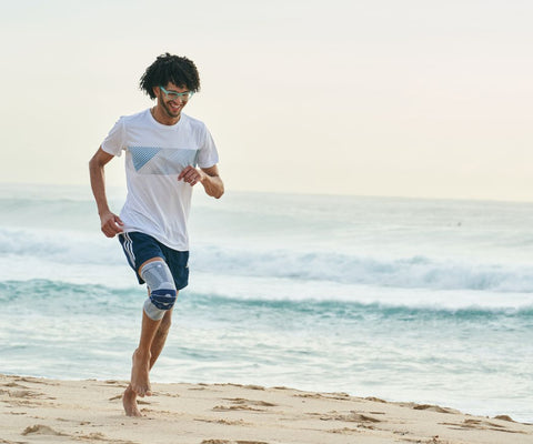 Man running on the beach in Bauerfeind's GenuTrain Knee Brace