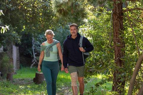 Man and woman waking along a trail through the woods on a cold but sunny day. The man is wearing Bauerfeind GenuTrain knee brace to combat his winter joint pain