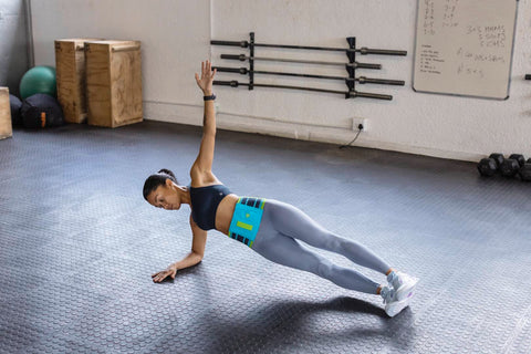 Woman doing a side plank at the gym while wearing Bauerfeind's Sports Back Support. Both are good ways avoid back injuries in sports like basketball