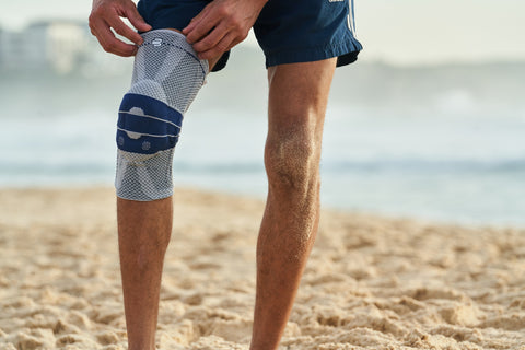 Man pulling on Bauerfeind's GenuTrain Knee Brace at the beach