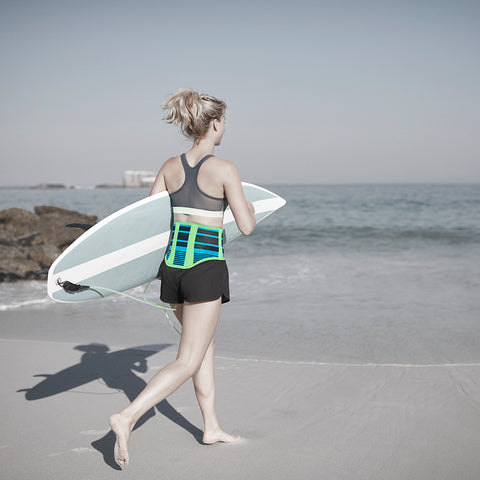 Woman on a beach walking toward the water while holding a surfboard. She is wearing a back brace, a surfing tip that will help keep her stable and help avoid back injuries.