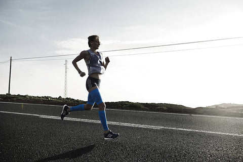 Woman in compression calf sleeves and compression thigh sleeves running along a road