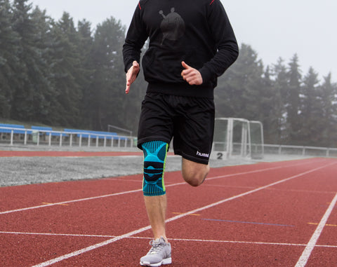 Man running along a sports track in a sports knee brace, a good piece of running gear to improve the way the knee tracks