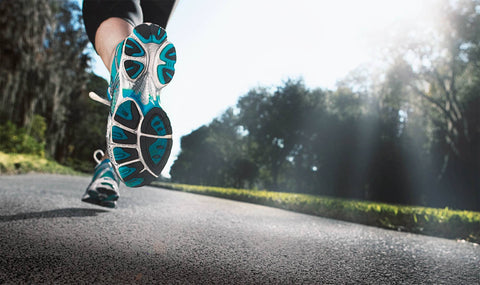 Man running on a road surrounded by forest. The shot focuses on his running shoes