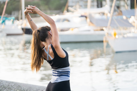 Woman stretching her back by the docks while wearing the LumboTrain back brace to stabilise her lumbar and relive pain