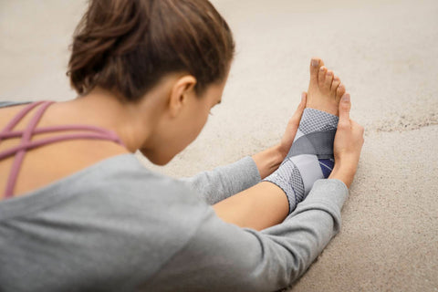 Over the shoulder shot of a ballerina sitting down and stretching her hamstring in Bauerfeind's MalleoTrain Plus Ankle brace