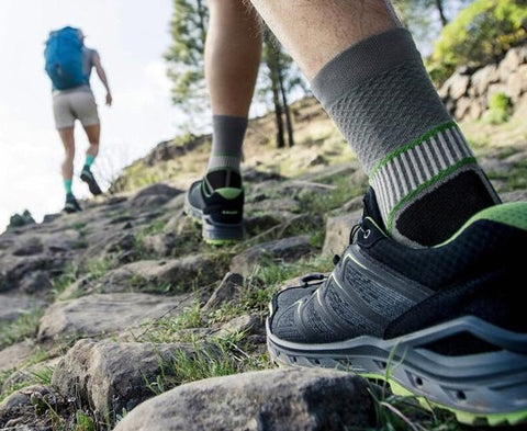 Woman and man trekking up a hill. The shot focuses on the man's foot and ankle, which is covered by Bauerfeind's mid cut compression sock for hiking 
