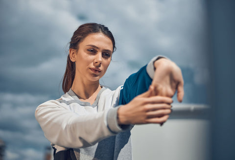 Woman doing the wrist extension stretch for carpal tunnel. Her arm is straight before her with the palm facing outward, and she's using her other hand to gently pull her hand further into the stretch