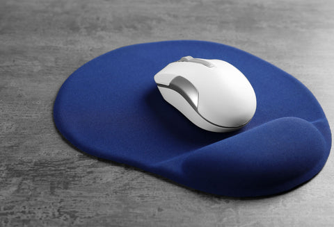 Mouse pad and a mouse on a wooden desk. The mouse pad has a little cushion for the wrist, making it a good and ergonomic fit for reducing the risk of wrist strain and syndromes like carpal tunnnel