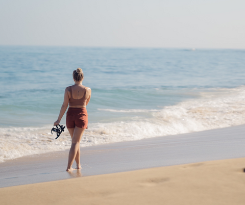 Wide shot of a woman strolling along a beach, a good activity to strengthen the feet