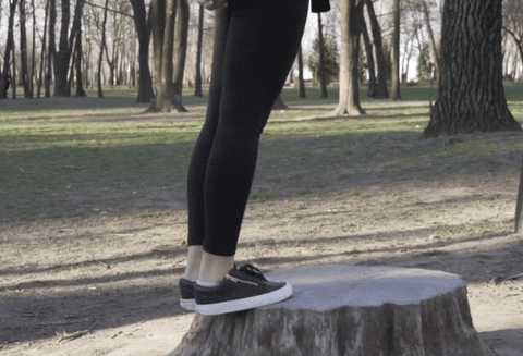 Woman in the woods doing calf raises on a tree stump. Calf raises are one of the best ways to strengthen the legs against the shin splints basketball injury