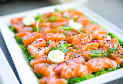 A square plate topped with raw salmon slices, leafy greens, and egg slices - all great foods to help the knee recover after surgery.