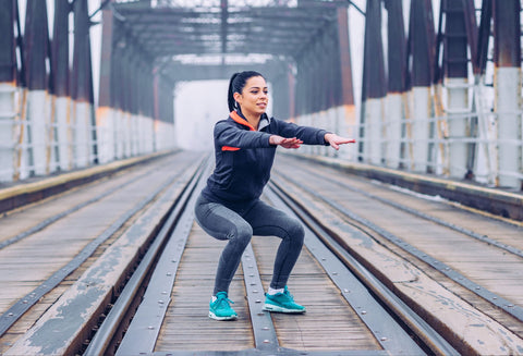 Woman on train tracks doing squats. She is doing so in the correct squat form to avoid knee pain