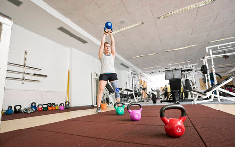 Person wearing a Bauerfeind knee brace lifting kettlebells in the gymphysiotherapy exercise