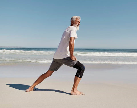 Older man doing lunges on the beach in Bauerfeind's GenuTrain OA knee brace, which is a good pick for moderate Osteoarthritis symptoms