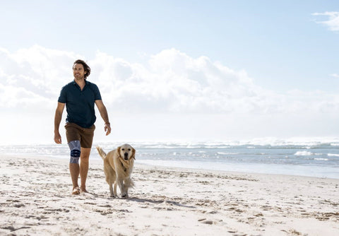 Man walking on the beach with his dog, a good exercise for knee pain.