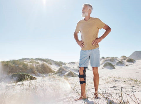 Older man standing on the beach in Bauerfeind's SecuTec OA Osteoarthritis knee brace. His hands are on his hips, and he looks to be smiling.
