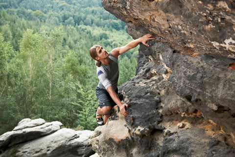 Man climbing a rock face while wearing Bauerfeind's OmoTrain shoulder brace to relieve pain