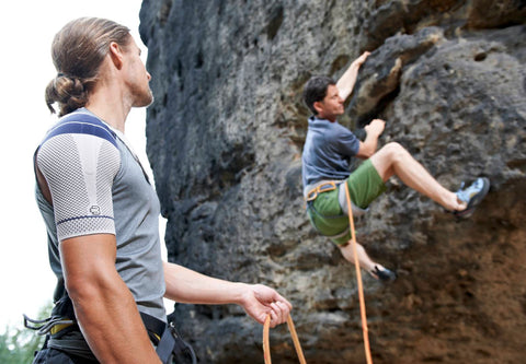 Man about to start rock climbing up a cliff. He is wearing Bauerfeind's OmoTrain Shoulder Brace, a great way to relieve shoulder pain from conditions like shoulder bursitis during exercise