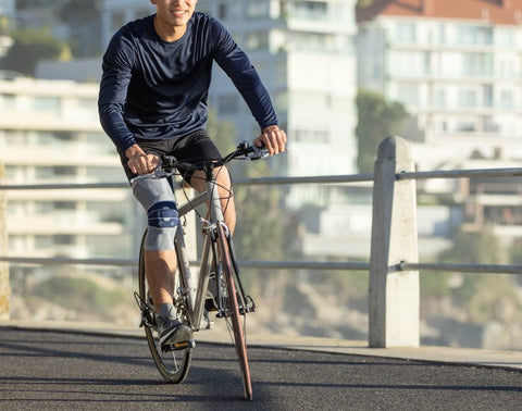 Man cycling along Bondi Beach wearing Bauerfeind's GenuTrain Knee Brace to manage knee pain