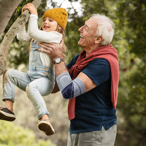 Older man holding up his granddaughter. He is wearing an EpiTrain Elbow Brace, a good way to relieve pain while recovering from minor elbow injuries. 