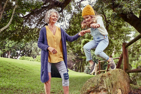 Older woman playing with her granddaughter at the park. The woman is wearing Bauerfeind's GenuTrain S Pro knee brace, which is helpful in regaining mobility after knee replacement surgery