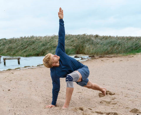 Man doing yoga on the beach while wearing Bauerfeind's GenuTrain Knee Brace, a great compression brace to improve proprioception